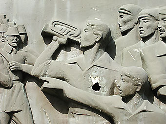 Kleiner Trompeter. Ausschnitt aus einem Relief auf dem Kasernengelände des MZOs (Mehrzweckobjekt). Das Relief ist aus Kunstharz. Zusammen mit dem Anstrich erweckt das Denkmal einen Bronze-Eindruck.