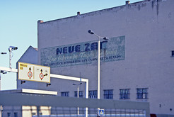 Hinweisschilder und Kamera am Grenzübergang Checkpoint Charlie auf der Friedrichstraße / Zimmerstraße im Bezirk Berlin-Mitte. Im Hintergrund Brandwand mit Werbeaufschrift für die "Neue Zeit", Parteizeitung der CDU in der DDR. Bild 9159